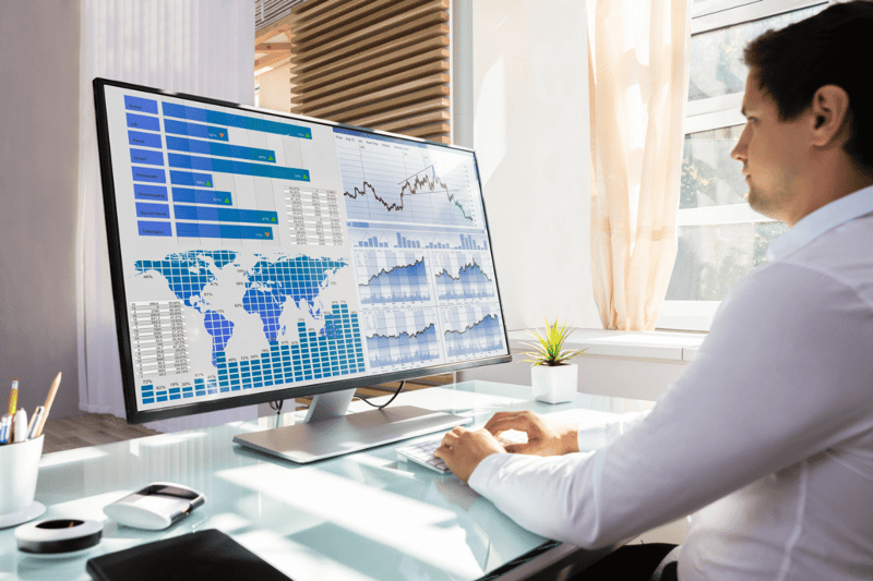 A Man Typing on a Keyboard and Looking at a Computer Screen with Maps Charts and Graphs on